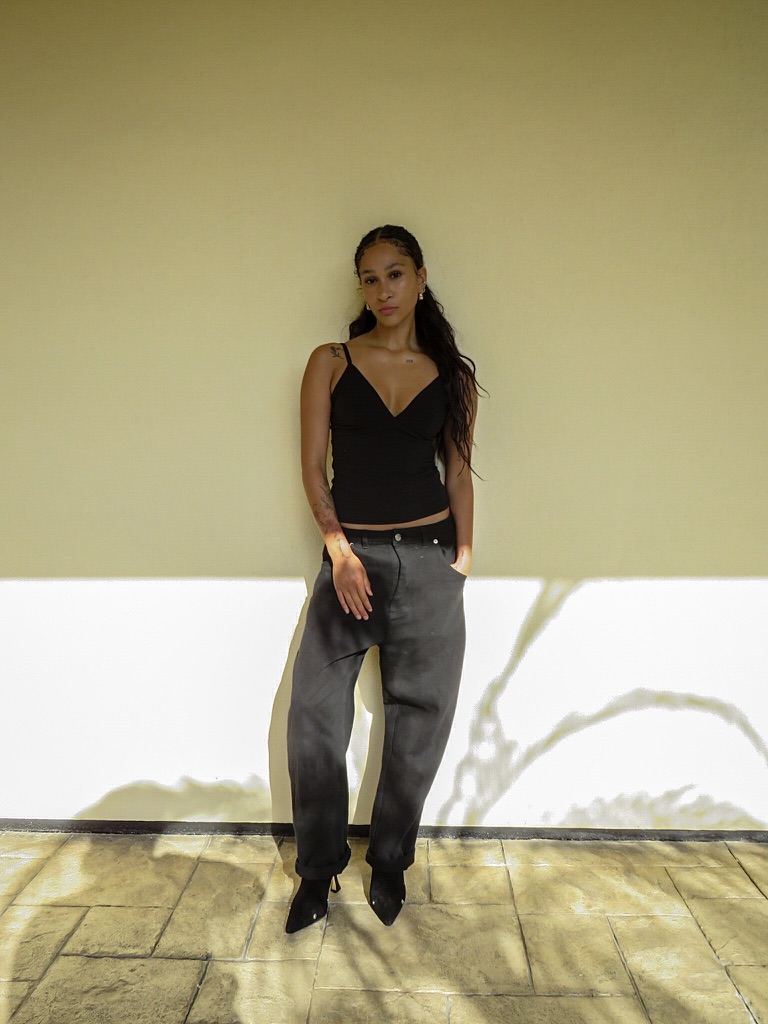 Digital — full-length front in black cami and grey jeans against a sunlit wall