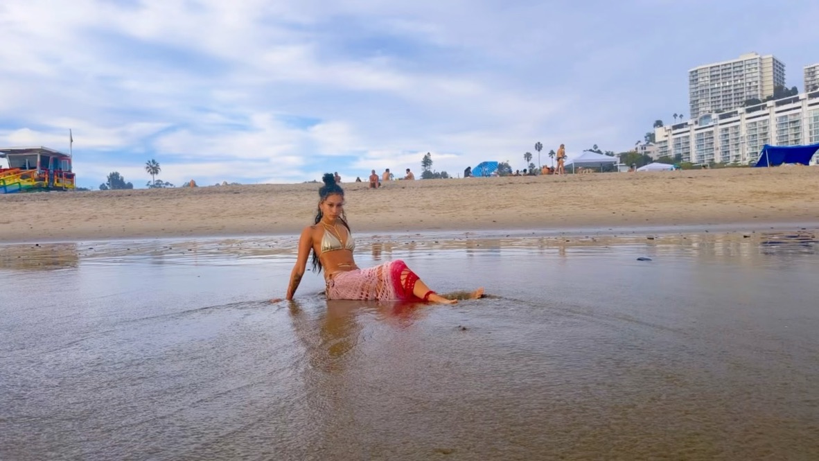 Maria Williams posed in the shallows in a gold bikini and pink crochet skirt beside a rainbow lifeguard tower