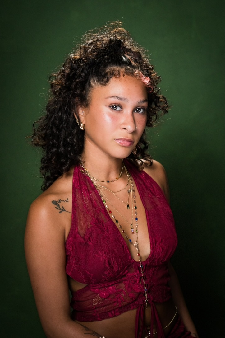 Studio portrait of Maria Williams in a burgundy lace halter with layered necklaces against a deep green backdrop