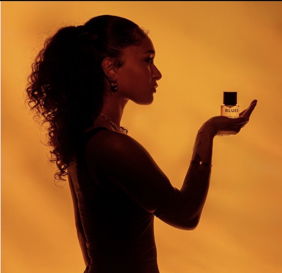 Silhouette of Maria Williams holding a Zernell Gillie "Blues" fragrance bottle against amber light
